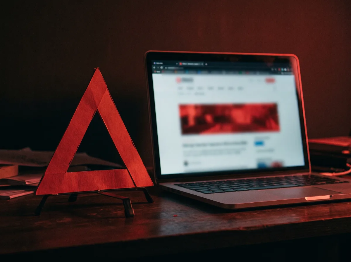 Symboliczna trójkątna flaga ostrzegawcza obok laptopa — ryzyko nielegalnego operatora